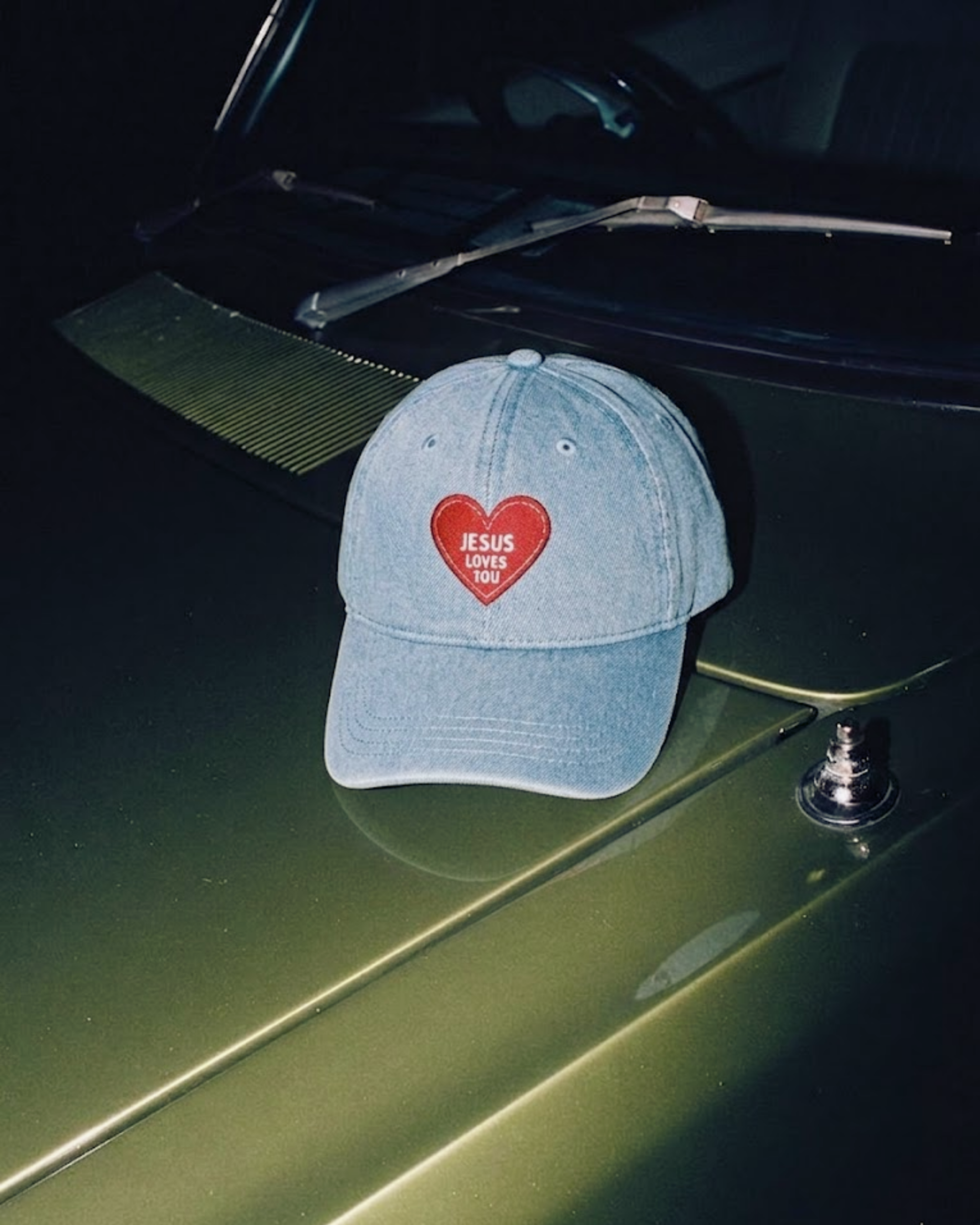 Jesus Loves You denim cap photographed on a green car